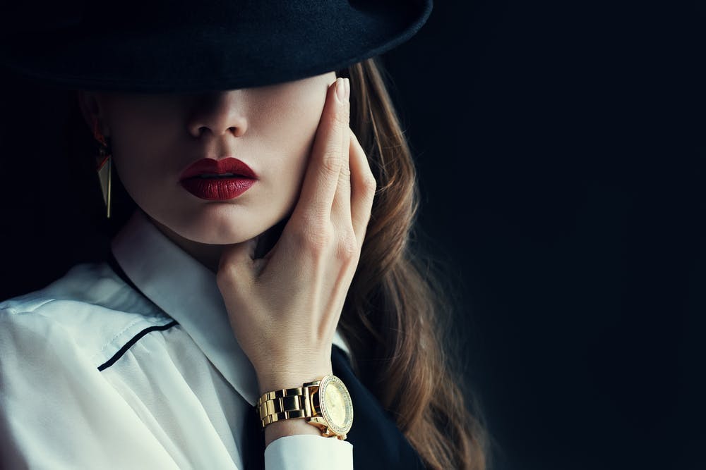 Portrait of a woman with black hat, red lips and a golden watch on her wrist